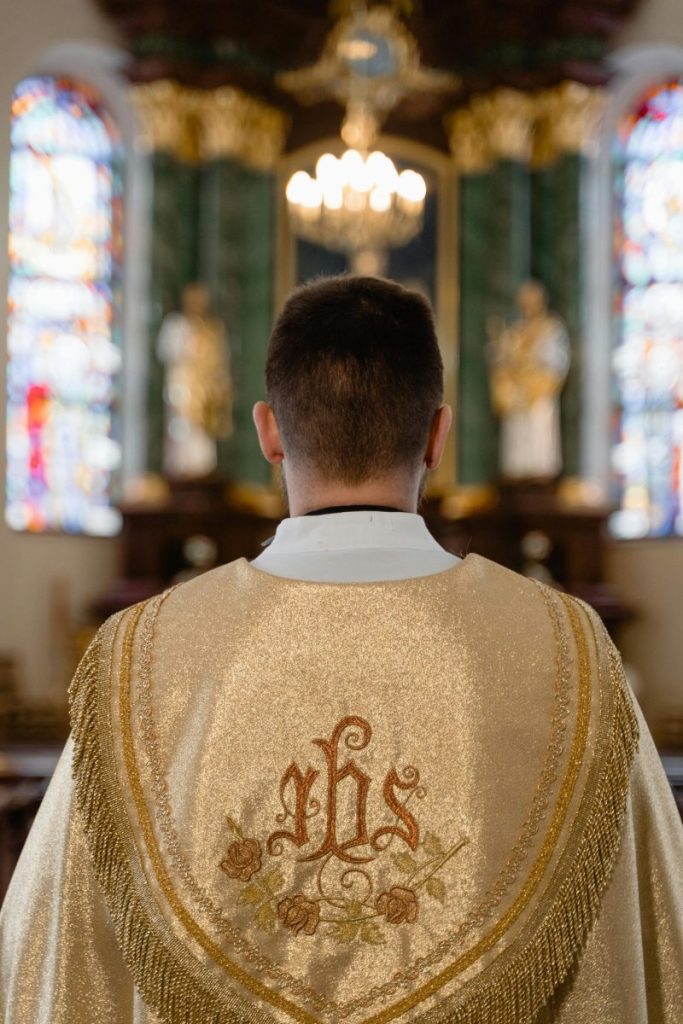 Back view of a priest in golden vestment, standing inside a cathedral during a religious ceremony.